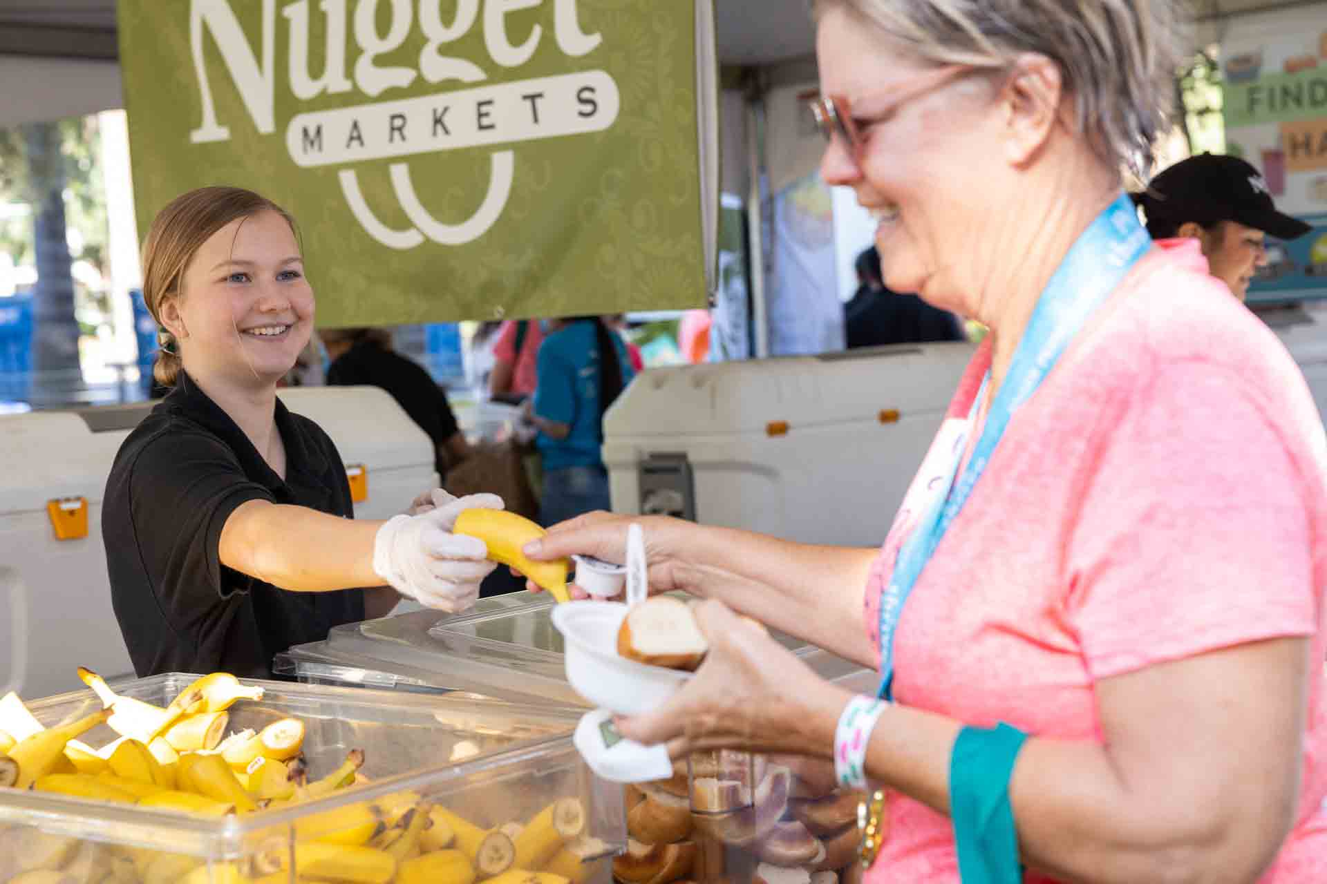 Nugget Markets associate handing a woman a banana at the Women’s Fitness Festival 2019